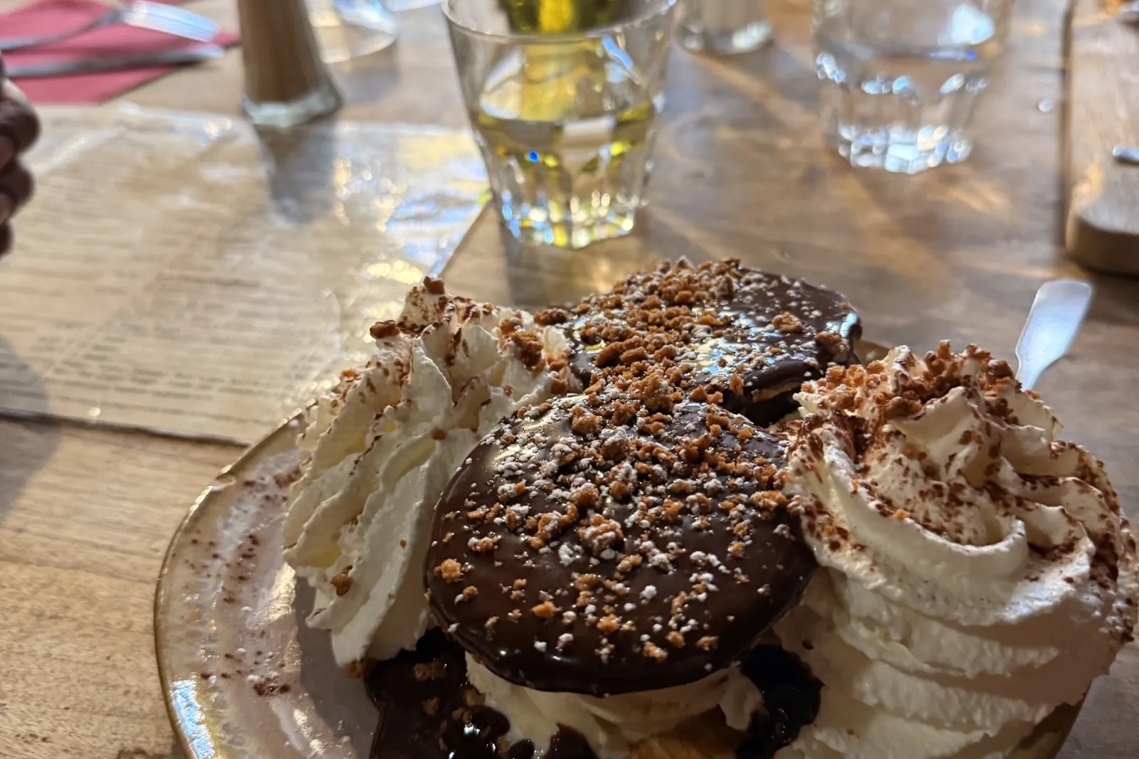 Un dessert au chocolat et à la chantilly, saupoudré d'éclats de spéculoos, sur une assiette de grès.