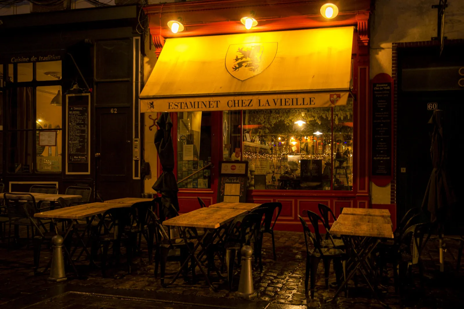 La devanture de Chez la Vieille la nuit, store jaune éclairé et terrasse rangée sur les pavés de la rue de Gand.