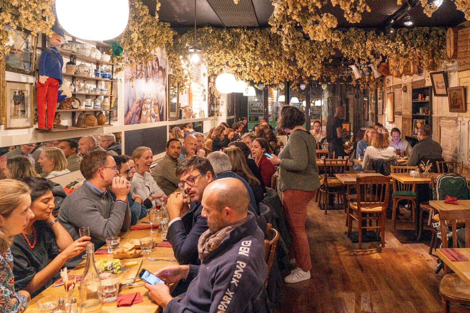 La grande salle un soir de service, houblon au plafond et tables de bois.